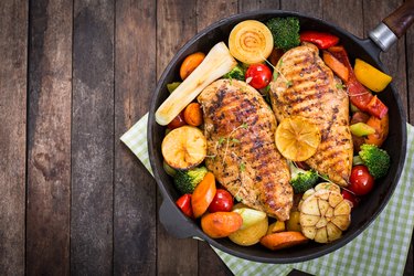 Protein-rich grilled chicken breast and vegetables in a skillet on green checkered cloth on wooden table
