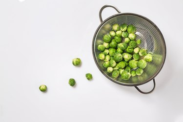 Colander with Brussels cabbage on white background