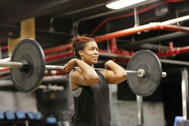 Fit, young African American woman working out with barbells in a fitness gym.