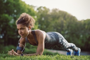Woman wearing headphones and doing an ab workout in the park.