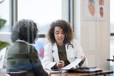 woman doctor in white coat reviews a patient's medical records in glass conference room