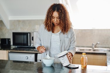 Woman scooping yogurt into bowl in kitchen