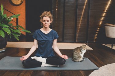 A woman sitting on a yoga mat with her cat and practicing 4-7-8 breathing