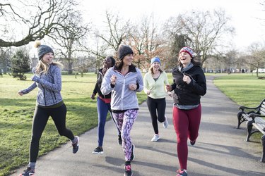 Smiling female runners running in sunny park