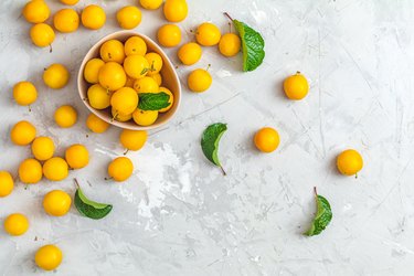 Creative summer pattern made of fresh yellow cherry plums in pink bowl on gray concrete background