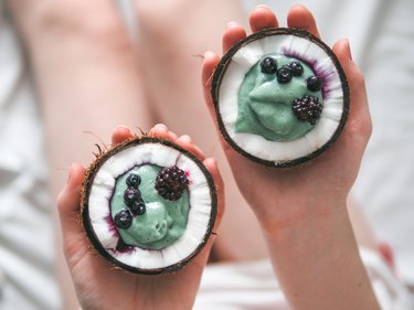 Two coconut half spirulina smoothie in woman hands