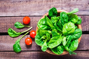 Fresh baby spinach leaves in a bowl and cherry tomatoes on a wooden table