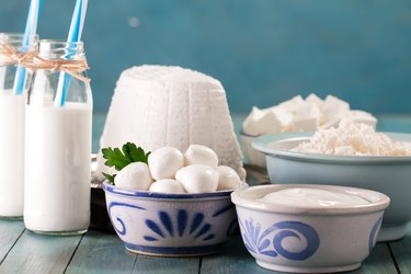 tasty healthy fermented dairy products on a table on a blue background: sour cream, cottage cheese, mozzarella cheese, butter,ricotta and milk in a bottle