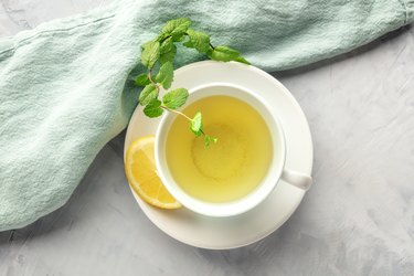 A cup of green tea with lemon and mint leaves.