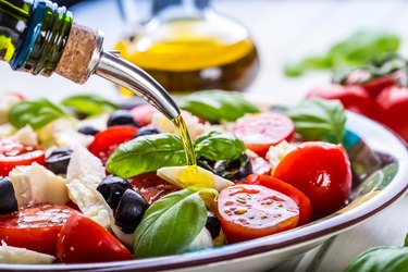 close up of a caprese salad with tomatoes, basil, mozzarella and olives with olive oil being poured on top