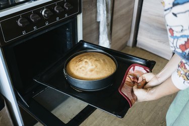 Midsection of woman preparing cake in oven at home