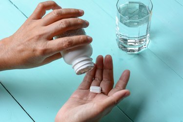 Person's hand pouring multivitamins into their palm with a glass of water sitting on a table