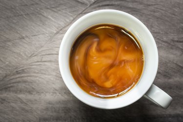 Cup of coffee with flowing milk on wooden background, overhead shot.