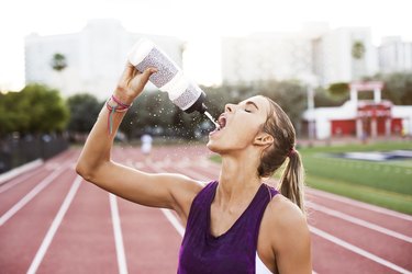 Female athlete drinking water on race tracks