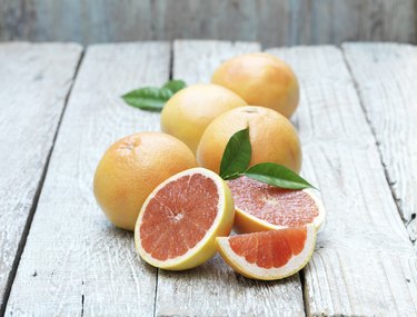 Whole and half pink grapefruit on whitewashed wooden table