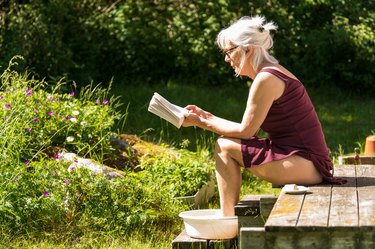 Woman sitting on porch reading a book and doing a foot soak for toenail fungus