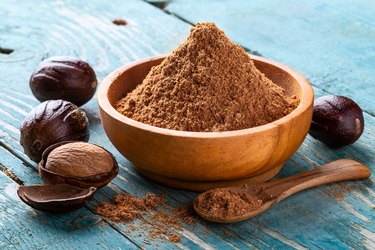 Whole inshell nut, cracked and nutmeg powder in a wooden bowl and spoon on old blue rustic background