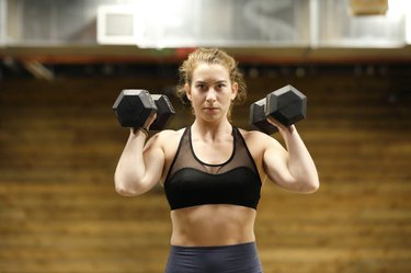 Fit, young woman working out with a dumbbells in a fitness gym with an intense look.
