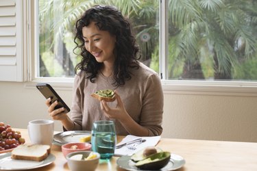 Young woman eating a healthy breakfast at home looking at her phone