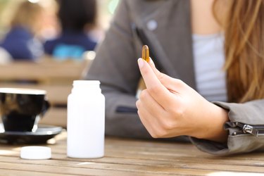 Woman showing vitamin pill on a coffee shop terrace