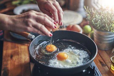 woman's hands cracking an egg into a frying pan, to represent foods high in protein for a healthy metabolism