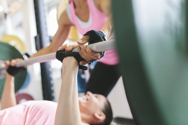 Two women doing barbell bench presses in a power rack