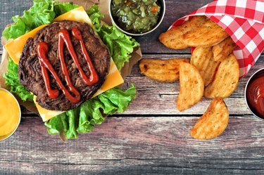 Picnic scene with hamburger and potato wedges over dark wood