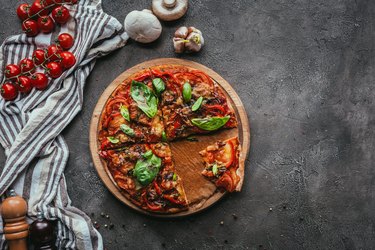 top view of freshly baked Whole Foods pizza on concrete table next to garlic cloves and cherry tomatoes