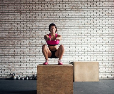 Concentrated woman squatting over a plyo box