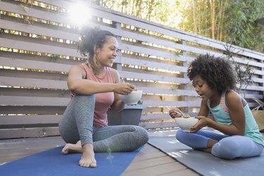 what to eat before a workout mother and daughter eating cereal on yoga mats on deck