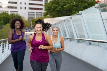 Three smiling women jogging together on a bridge