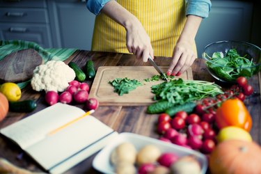 A woman in a yellow apron cutting up a variety of fresh vegetables in the kitchen, as an example of foods on the mayo clinic diet