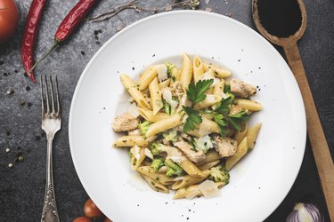 Vegetarian penne pasta with broccoli and parsley in a white bowl over charcoal background.