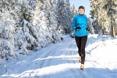 青年女子在森林中雪覆盖路上运行