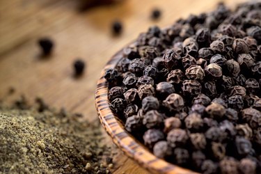 Close view of black peppercorns in a wooden bowl