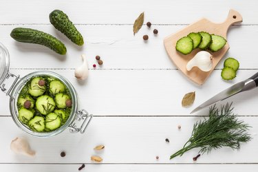 Cucumbers ready for pickling and ingredients on white table.