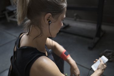 Woman weightlifting, resting and listening to music with headphones and mp3 player at gym