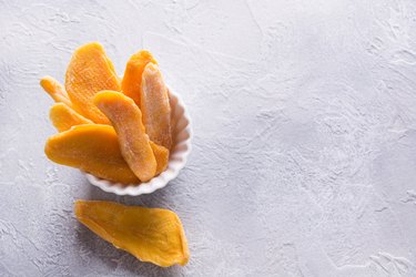 Dehydrated and dried mango chips in white bowl. Close up.