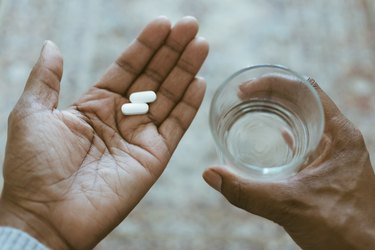 Close-Up View of Hands Holding a glass of water and two pain reliever pills, as a stye remedy