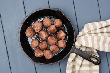 Homemade beef meatballs fried in cast iron pan with flax cloth on gray wooden table