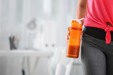 Young woman holding bottle with protein shake indoors
