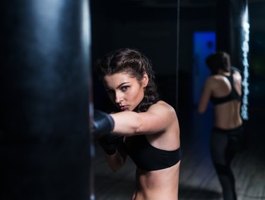 Young fighter boxer girl in training with heavy punching bag