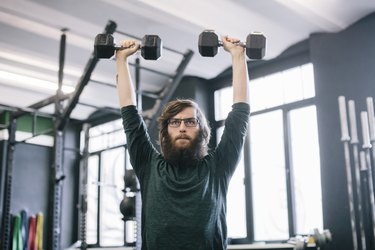 Man doing a shoulder press with dumbbells at the gym