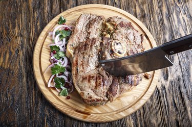 cooked beef steak on a round cutting board. next to it is chopped onion and parsley.