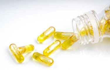 Close-Up Of Yellow Vitamin Capsules Spilling From Bottle Over White Background