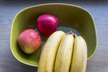 Fresh apples and bananas on green bowl