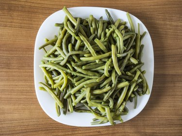 White plate of green beans boiled on a wooden table. Spain