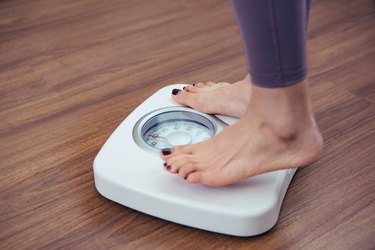 A person stepping onto a white bathroom scale to weigh themselves.