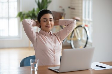 Peaceful young woman relaxing with closed eyes doing breathing exercises with laptop