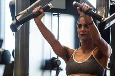 Muscular young woman strength training her upper body on chest press